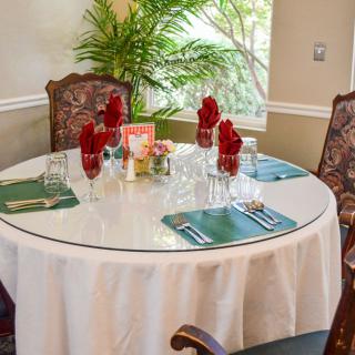 An elegantly set round dining table with red napkins and greenery in a cozy indoor restaurant.