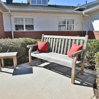 A wooden bench with red cushions on a sunny patio.