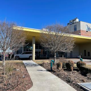 A modern building with a yellow roof and surrounding greenery under a clear blue sky.