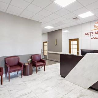 A modern reception area with maroon chairs, a dark desk, and marble flooring.