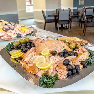 A beautifully arranged buffet platter featuring slices of salmon garnished with lemons, olives, and greenery.