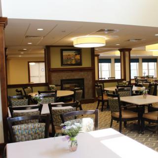 A cozy dining room with arranged tables and chairs, featuring warm lighting and wood accents.