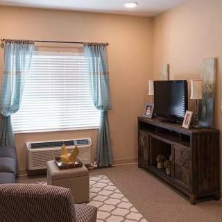 A cozy living room with a television, comfortable seating, and light blue curtains by the window.