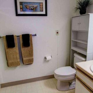 A neatly organized bathroom with a toilet, towel rack, storage shelf, and artwork on the wall.