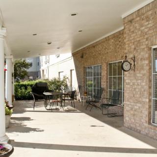 A covered patio area with tables and chairs alongside a brick wall and large windows.