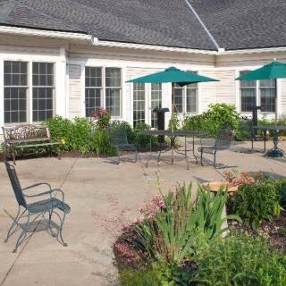 A sunny patio with chairs, tables, and garden umbrellas surrounded by lush greenery.
