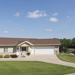 A single-story ranch-style house with a large front lawn and a two-car garage under a clear blue sky.