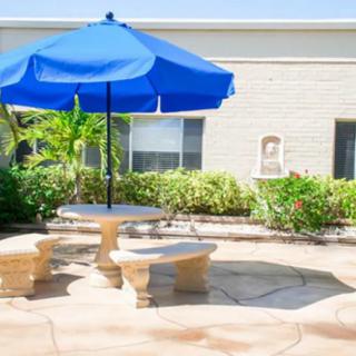 A sunny patio setting with a blue umbrella over a stone table and benches.