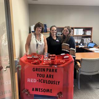 Three people standing behind a red-themed display in an office with a sign expressing appreciation.