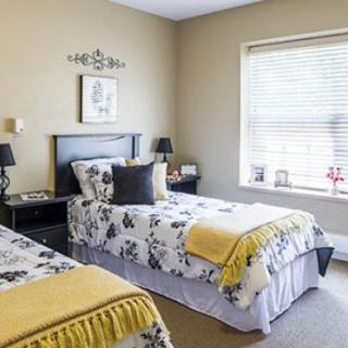 A well-decorated bedroom with two twin beds featuring floral bedding and yellow accents, complemented by a large window allowing natural light.