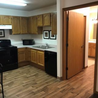 A modern apartment kitchen with wooden cabinets and black appliances.