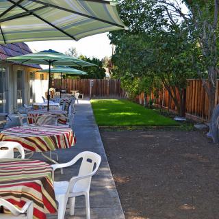 A backyard patio with tables, umbrellas, and chairs next to a garden and a wooden fence.