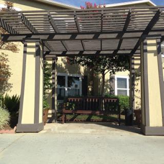 A welcoming entrance featuring a pergola and a bench, surrounded by greenery.