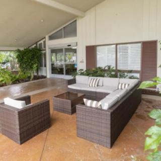 A modern outdoor patio featuring wicker furniture with cushioned seating, surrounded by plants.