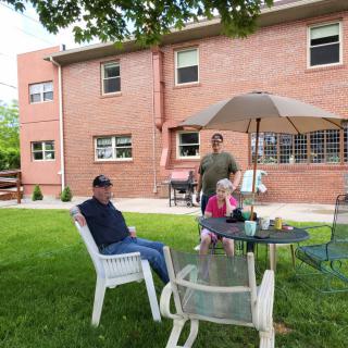 A group of people relaxing in a backyard with lawn chairs and a patio set in front of a brick house.