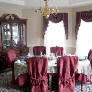 A formal dining room with a decorated table, elegant chandelier, and red chair covers.
