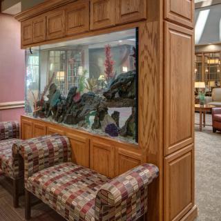 A cozy lobby features a large fish tank integrated into wooden cabinetry, flanked by patterned chairs.