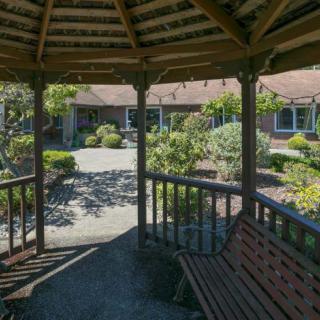 A serene view from inside a gazebo overlooking a lush garden with a bench.