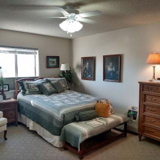 A cozy bedroom with a neatly made bed, dresser, and decorative elements such as paintings and a lamp.