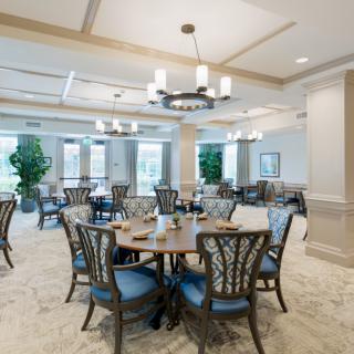 An elegant dining room with neatly arranged tables and chairs, featuring chandeliers and tasteful decor.