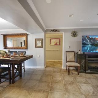 A cozy living room with a dining area, featuring a TV, wooden table, chairs, and various decorative elements.