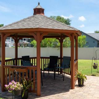 A wooden gazebo with patio furniture set in a sunny backyard garden.