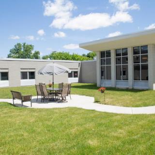 A courtyard with patio furniture and an umbrella beside a modern building under a clear blue sky.