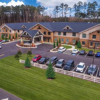 Aerial view of a residential building with a parking lot surrounded by trees and grass.