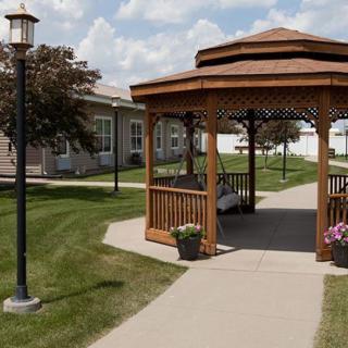 A wooden gazebo along a landscaped pathway with neatly trimmed grass and potted plants.