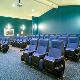 An empty movie theater with rows of blue seats and a projector screen.