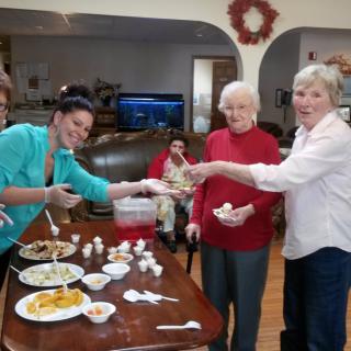 A group of people enjoying food together indoors, smiling and serving themselves from a table filled with dishes.