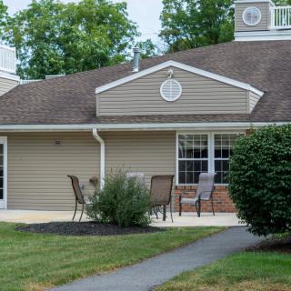A residential house with a patio, outdoor chairs, and surrounding shrubs.