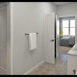 A view from a bathroom into a bedroom, with a towel on the wall and natural light coming through the windows.