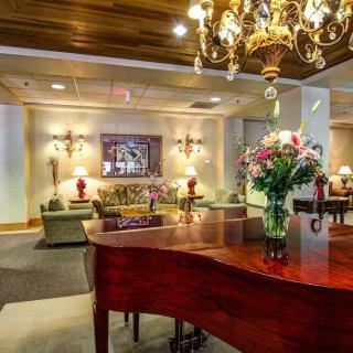 A luxurious hotel lobby featuring a grand piano, elegant chandelier, and comfortable seating area adorned with flowers.