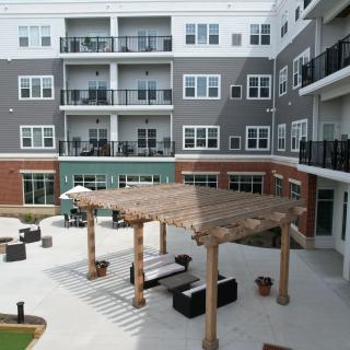 A modern apartment complex with a central patio area featuring outdoor seating and a pergola.