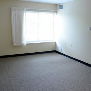 A bright, empty room with neutral walls and a large window allowing natural light.