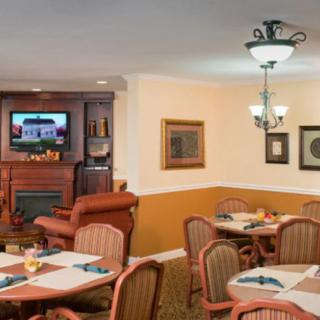 A cozy dining area with several tables and chairs, featuring a fireplace and a television.