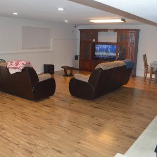 Spacious living room with hardwood flooring, featuring cozy sofas and a television setup, adjacent to a dining area.