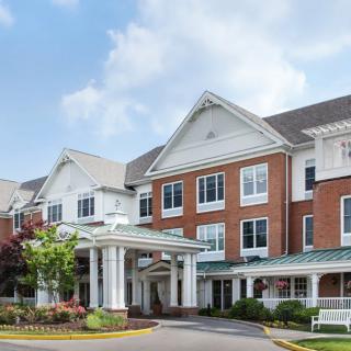 A picturesque view of a large residential building with traditional architecture, featuring a brick facade and white columns at the entrance under a clear blue sky.
