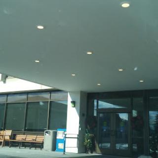 The entrance of a modern building featuring large windows and outdoor seating.