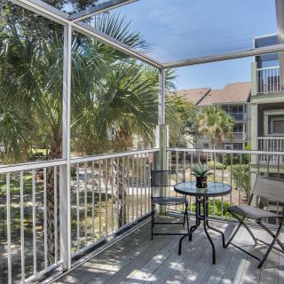 A cozy balcony with a small table and chairs overlooking palm trees and apartments.