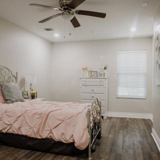 A minimalist bedroom with a metal bed frame, wooden dresser, and ceiling fan.
