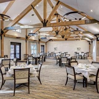An elegant restaurant interior with neatly arranged tables and chairs, featuring exposed wooden beams.