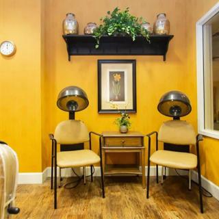 A cozy salon waiting area with two chairs, hair dryers, and decorative elements on a warm-toned wall.