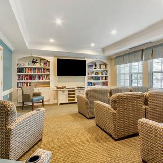 A cozy living room with comfortable armchairs facing a large television, flanked by bookshelves and well-lit by natural light from the windows.
