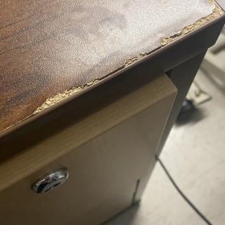 A close-up of a damaged wooden desk corner in an office setting.