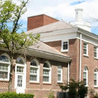 A classic brick building with arched windows and a tree in the foreground.