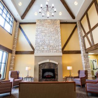 A spacious living room featuring a large stone fireplace, high ceilings with wooden beams, and a chandelier, complemented by comfortable seating.