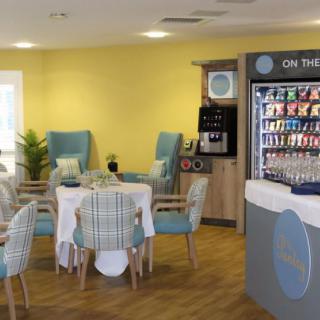 A cozy indoor cafe space with tables, chairs, and a vending machine.