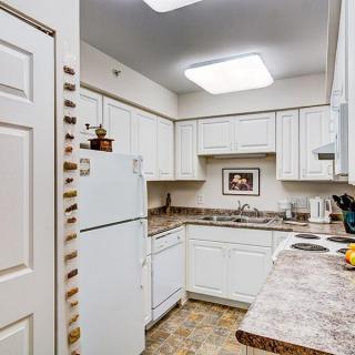 A compact kitchen space featuring white cabinets, a refrigerator, and a countertop with various kitchen items.